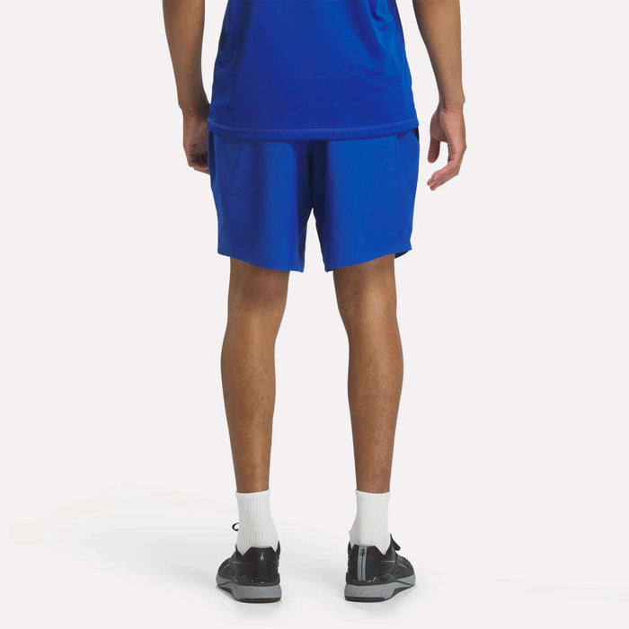 A person wearing a blue shirt, Men's Reebok x F45 Training Woven Shorts, white socks, and black sneakers stands with their back to the camera against a plain white background—ready for high-intensity training.