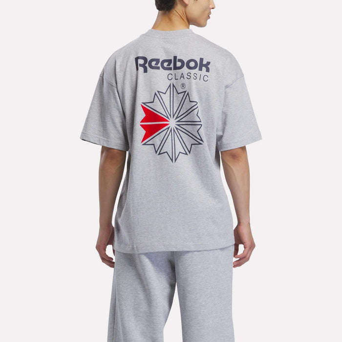 A person is seen from behind wearing the Reebok Men’s Relaxed Logo T-Shirt in gray—a classic cotton tee featuring a large logo and a red accent on the back—paired with matching gray pants.