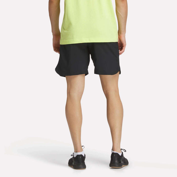 A person stands facing away, wearing a light green T-shirt and Reebok Men's Run Shorts with inner tights, paired with black athletic shoes, against a plain white background.