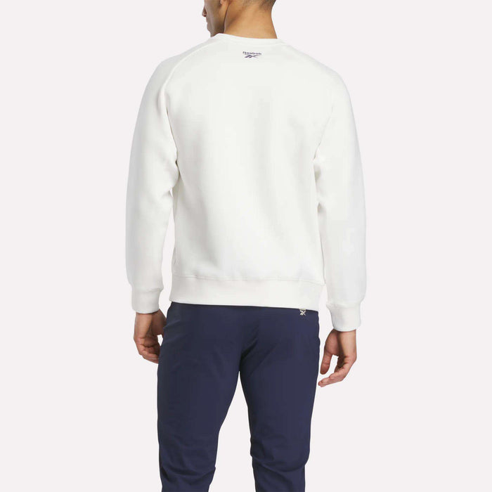 A man faces away from the camera, wearing a white Reebok Men's Scuba Knit Crew Sweatshirt and navy blue pants against a plain light background.