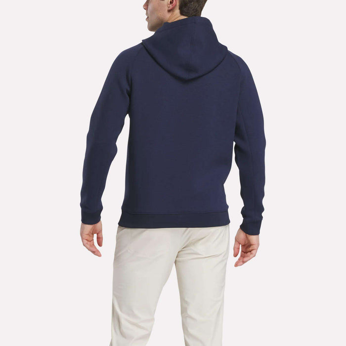 A man is seen from the back wearing a navy blue Reebok Men's Scuba Knit Hoodie Sweatshirt and light pants, set against a plain white background.