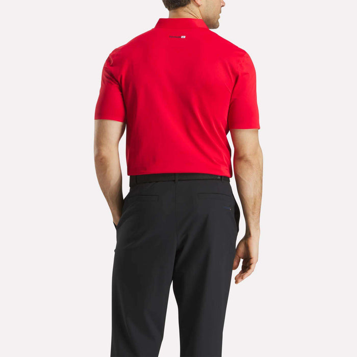A man, seen from the back, wears a bright red Reebok Men's Short Sleeve Bonded Micro Pique Polo Shirt with black pants. His right arm is by his side and his left hand is in his pocket, standing out against a plain white background.