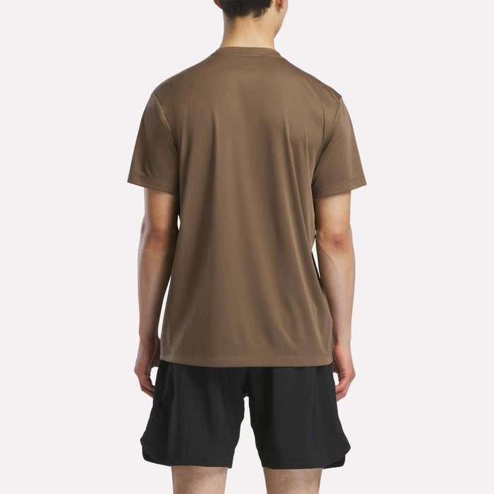 A person faces away from the camera wearing a brown Reebok Men's Short Sleeve Tech Training T-Shirt and black shorts against a plain light background.
