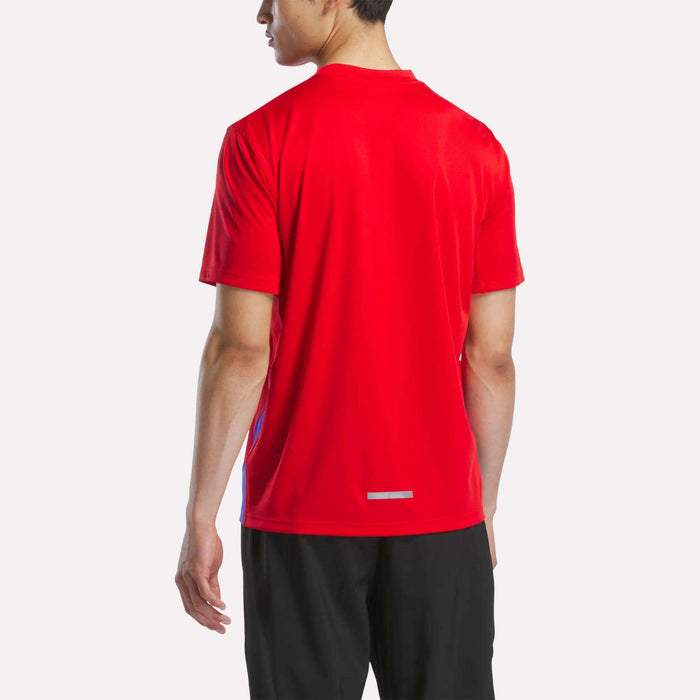 A man faces away from the camera, wearing a bright red Reebok Men's Short Sleeve Vector T-Shirt and black shorts, set against a plain light background.