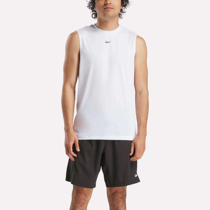 A man stands facing forward wearing a Reebok Men's Sleeveless Tech Training T-Shirt and black shorts with a small logo, set against a plain light background.