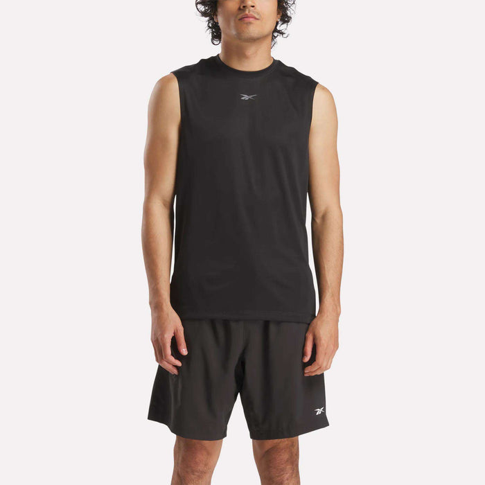 A man stands facing forward against a white background, wearing Reebok's Men's Train Sleeveless Tech Tee and black shorts, both with a small white Reebok logo that highlights their lightweight polyester construction.