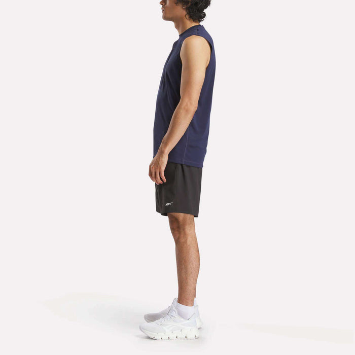 A man in profile wears a Reebok Men's Train Sleeveless Tech Tee in navy, black athletic shorts, and white sneakers against a plain white background.
