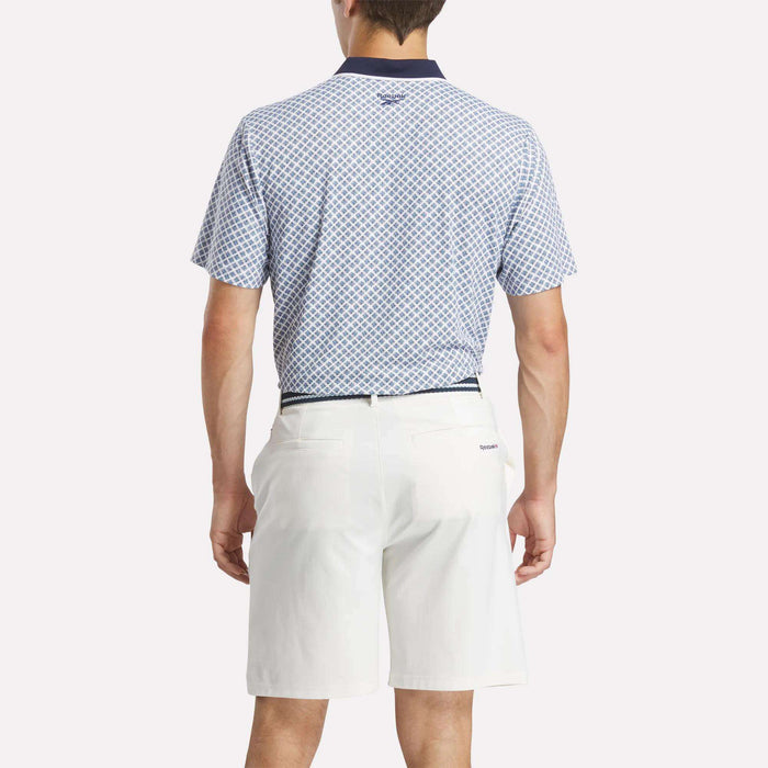 A man, seen from behind, wears a light blue Men's Sublimation Print Shirt by Reebok with sweat-wicking technology and white knee-length shorts. The background is plain white.