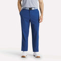 A man stands with his hands in his pockets, wearing a light gray striped polo, white sneakers, and Reebok Men's The Favorite Golf Pants - Relaxed Fit in blue with a black and gray belt against a plain background.