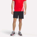 A person wearing a red short-sleeve athletic shirt, Reebok Men's Train Blocked Knit Shorts in black, and gray running shoes stands against a plain white background. The image is cropped just below the shoulders.