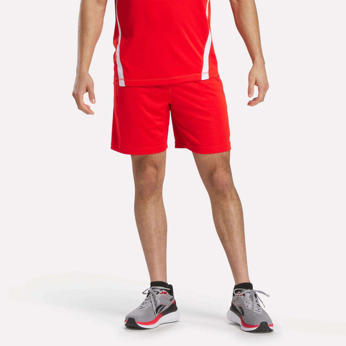 A person models Reebok Men's Train Blocked Knit Shorts, paired with a red athletic shirt and gray running shoes with red accents, against a plain white background. The head is cropped out—ideal for focusing on the workout wear.