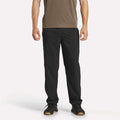 A person wearing a brown short-sleeve shirt, Reebok Men's Train Woven Unlined Pants, and black sneakers stands facing forward against a plain white background.
