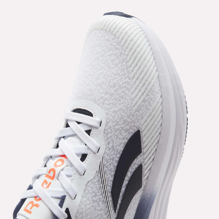 Close-up of a white Reebok Men's Viva Speed Shoe featuring black stripes, a gray knit texture, and orange Reebok branding on the tongue. Designed for ultimate comfort, these shoes include white laces, a thick cushioned sole, and a breathable knit construction—making them ideal for active lifestyles.