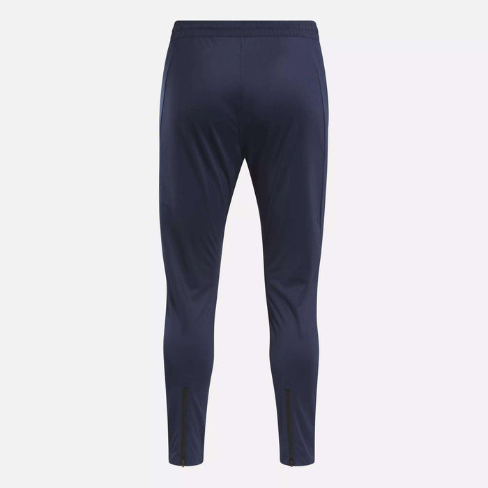 The Reebok Men's Workout Ready Track Pant in navy blue features a slim fit, elastic waistband, and ankle zippers—ideal as workout pants for any training session. Shown from the back.