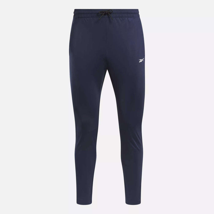 The Men's Workout Ready Track Pant by Reebok in navy blue features an elastic waistband, drawstring, and a small white Reebok logo on the left thigh, shown against a plain white background.