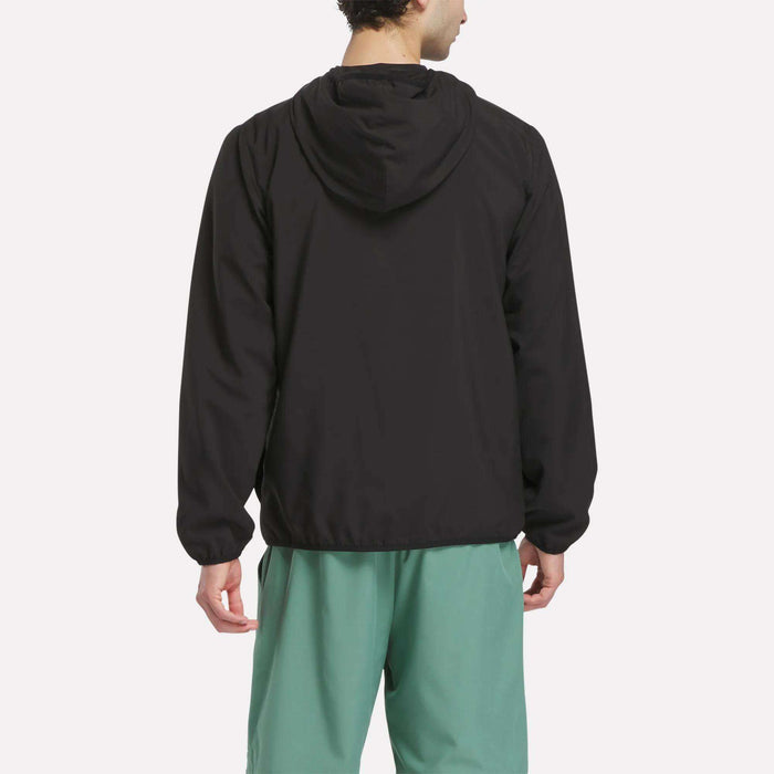 A person is shown from the back, wearing a relaxed fit black Reebok Men’s Woven Jacket and green shorts, standing against a plain white background.