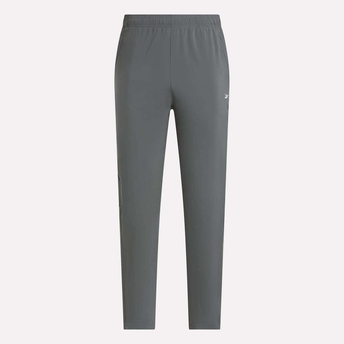 Reebok Men's Woven Pants in gray with an elastic waistband, tapered legs, and a small white logo on the thigh. These lightweight polyester training pants are shown against a plain light background.