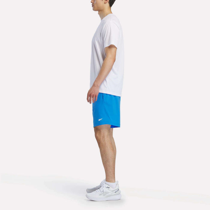 Side view of a man wearing a white t-shirt, Reebok Men's Woven Shorts in blue, and white athletic shoes.
