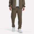 A person wearing Reebok Men’s Woven Training Pants in army green, paired with a white shirt and white sneakers, standing against a plain white background.
