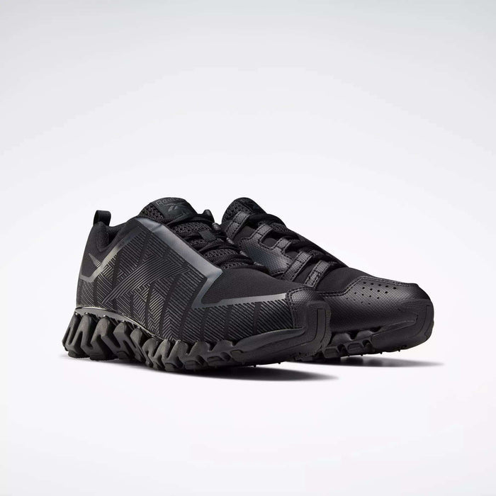 A pair of Reebok Men's ZigWild Trail 6 Shoes in black, with textured soles, geometric side patterns, and enhanced cushioning, displayed on a plain light background.