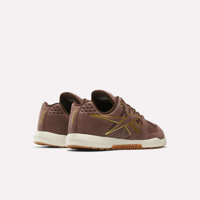 The Reebok Nano 2.0 Training Shoes feature brown pebbled leather, gold accents, gum soles, side logo, and perforated heel details; pictured from back and side angles on a plain white background.