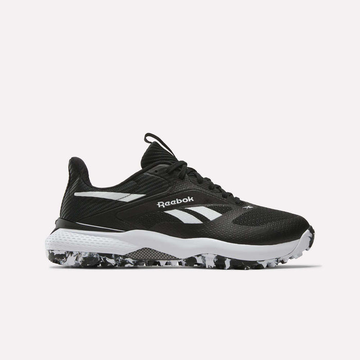 The Reebok Nano Golf Shoes feature a black FlexWeave upper, white detailing and logo, a white midsole, and a black-and-white speckled outsole, displayed on a plain light background.