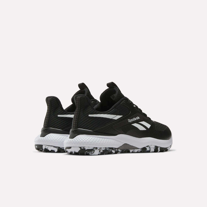 A pair of Reebok Nano Golf Shoes with a black FlexWeave upper, white accents, a white midsole, and a black-and-white marbled outsole is displayed against a plain white background.
