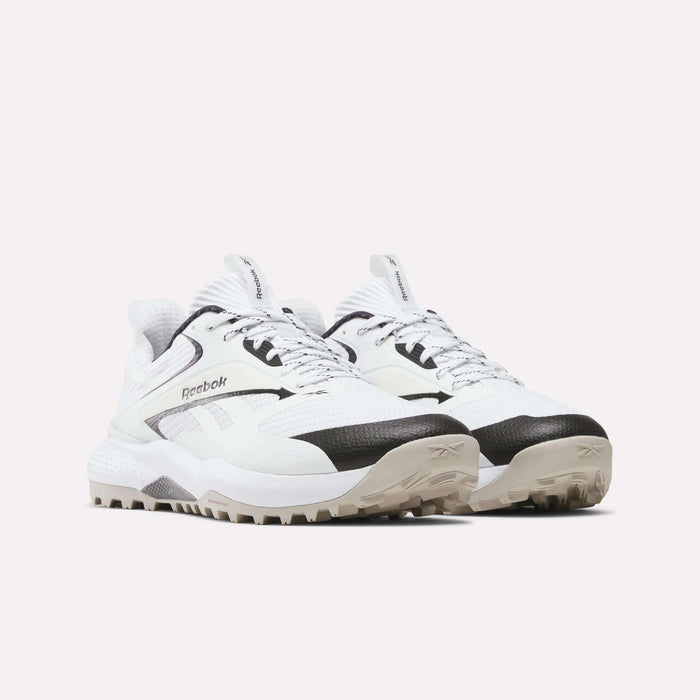 A pair of Reebok Nano Golf Shoes featuring a FlexWeave upper, black and white colorway, beige rugged soles, side logo details, and textured materials, displayed side by side on a plain light background.