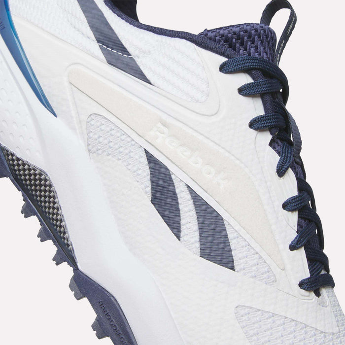 Close-up of Reebok Nano Golf Shoes in white and navy, featuring a lightweight FlexWeave upper, blue and black accents, dark blue laces, and visible Reebok branding on the side.