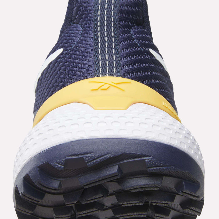 Close-up front view of the Reebok Nano Golf Shoes in navy blue with a textured white sole, yellow accent above the toe, white center stitching, and visible tread. Features include a lightweight FlexWeave upper for added comfort.