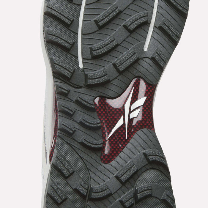 Close-up of Reebok Nano Golf Shoes sole featuring a rugged grey tread, red and black carbon fiber midsection, and white logo—designed for performance with a lightweight FlexWeave upper for optimal comfort.
