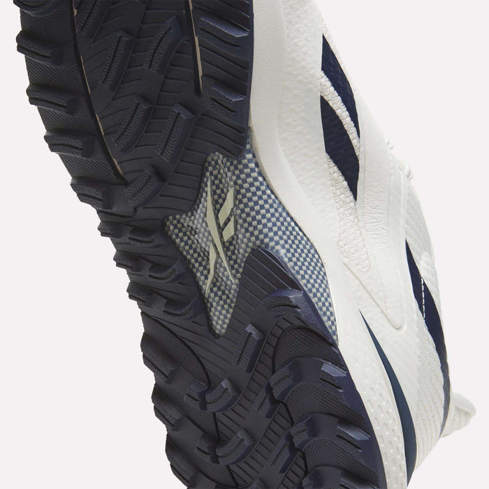 Close-up of the sole of the Reebok Nano Golf Shoes, showcasing a black, white, and blue color scheme with a textured grip and a visible Reebok logo on the midfoot area. The innovative Floatride foam offers lightweight cushioning inspired by performance golf shoes.