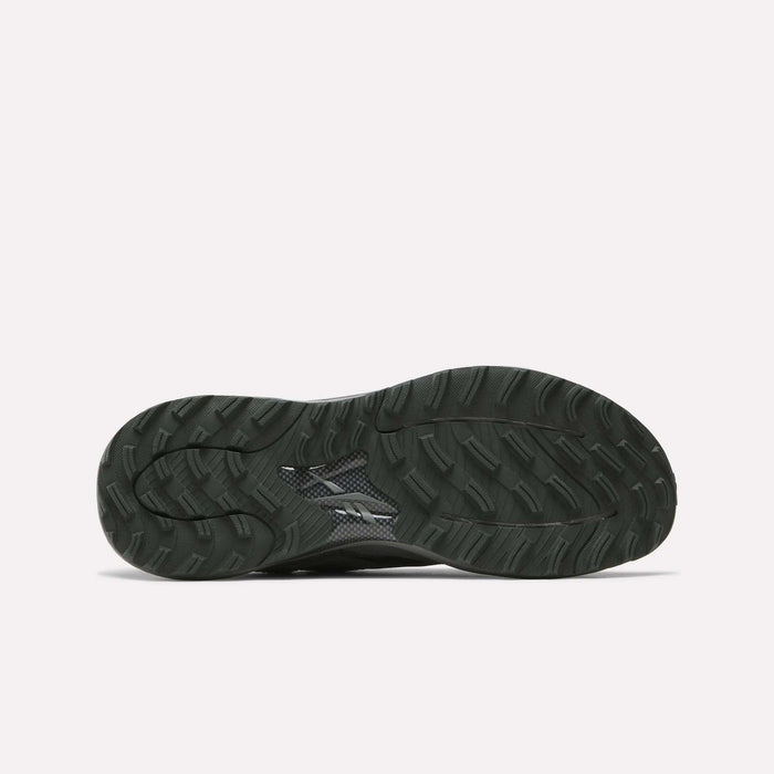 The image shows the black, textured rubber outsole of Reebok's Nano Golf Shoes with a wavy tread pattern and small logo near the center, designed to complement its lightweight FlexWeave upper. The background is plain white.