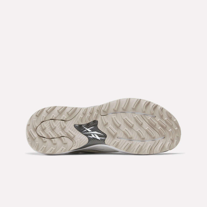 The image shows the sole of Reebok Nano Golf Shoes, featuring a beige, textured tread with a black middle section displaying a white logo—highlighting the comfort of Floatride foam. The background is plain and light-colored.