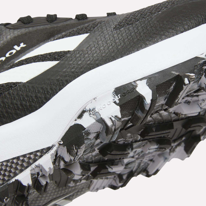 Close-up of Reebok Nano Golf Shoes in black and white, highlighting the textured sole with rugged tread pattern and FlexWeave upper for enhanced durability, plus a visible white logo.