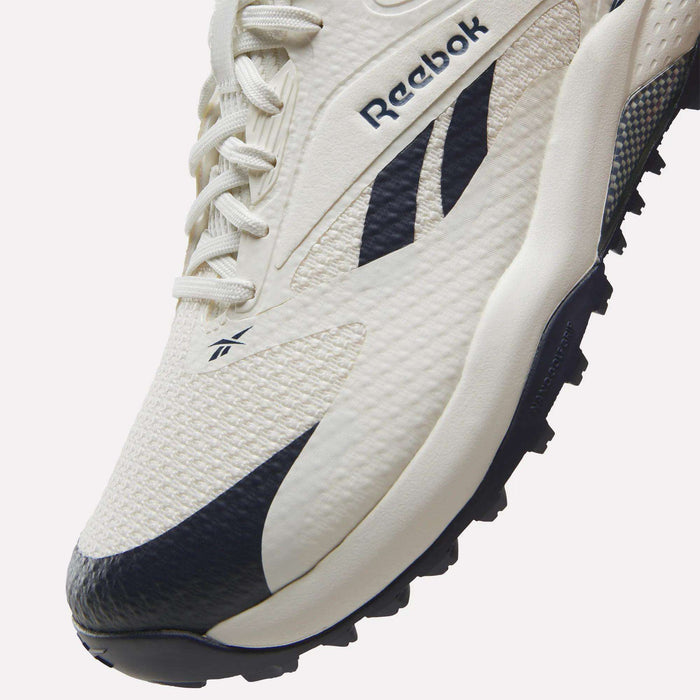 Close-up of a white Reebok Nano Golf Shoe with black accents, showcasing the textured material, laces, Reebok logo, and detailed stitching on the side and toe area—highlighting innovative Floatride foam for cushioned comfort found in today’s lightweight golf shoes.