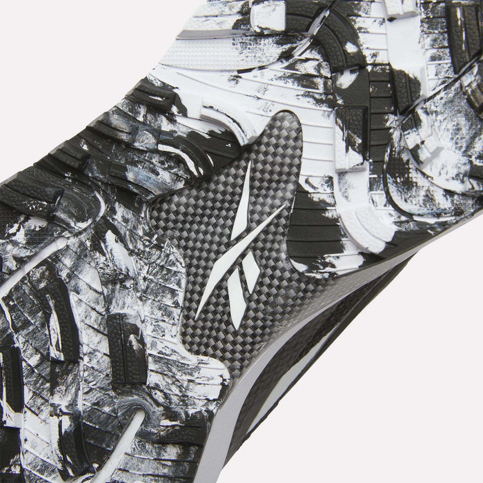 Close-up of the Reebok Nano Golf Shoes sole, showing a textured black and white pattern with a central Reebok logo. Rugged, angular tread shapes enhance traction, while performance foam offers comfort on the course.