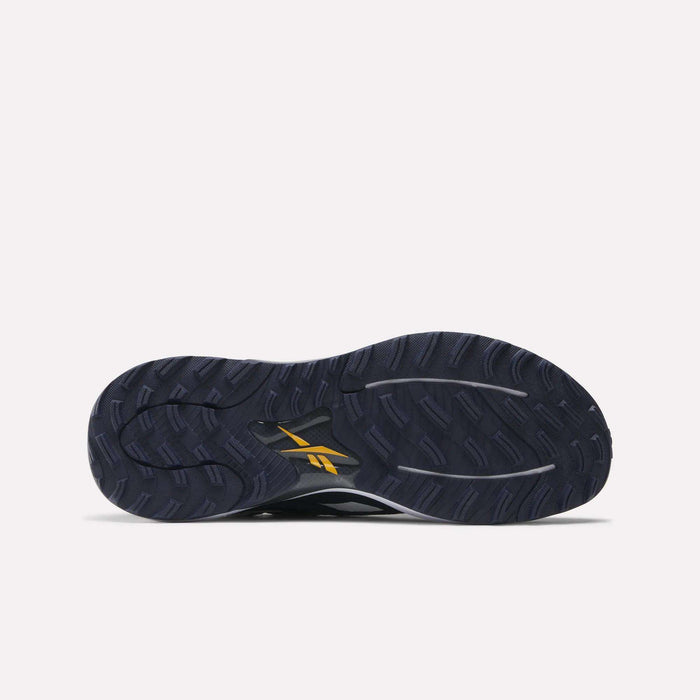 The image shows the bottom of a dark navy Nano Golf Shoe by Reebok with a textured tread, a yellow Reebok logo near the sole’s center, and Floatride performance foam for enhanced comfort.