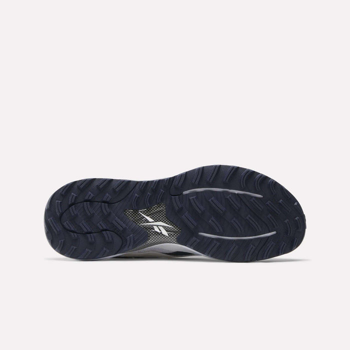The image shows the dark blue, textured rubber outsole of Reebok Nano Golf Shoes with deep grooves for traction and a white Reebok logo in the center. This pairs with a lightweight FlexWeave upper for support and comfort, set against a light gray background.
