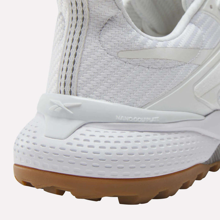 Close-up of the heel of a white Reebok Nano Golf Shoe with textured patterns, tan rubber outsole, and embossed Reebok logo. "NANO COLPLATE" above the midsole highlights its lightweight FlexWeave construction.