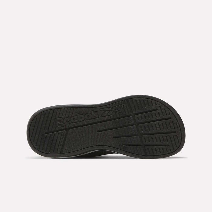 The image shows the black rubber outsole of the Reebok Nano Play Stretch Lace And Top Strap Shoes for little kids, with textured grip patterns and an embossed Reebok logo featuring the brand's vector symbol in the center.