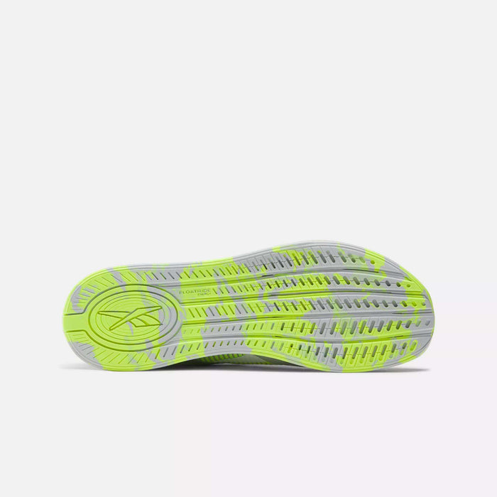 The image displays the sole of Reebok Nano X4 Training Shoes in neon yellow with gray accents and tread patterns. A stylized logo appears on the heel, set against a plain, light-colored background.