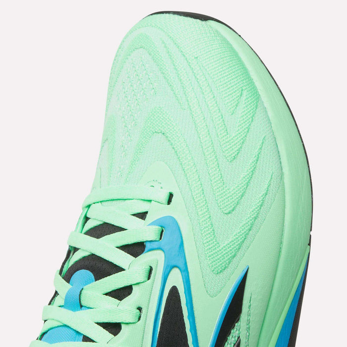 Close-up of the front and side of a light green Reebok Nano X5 Edge Training Shoe with black, blue, and green laces. The toe features wavy textures in Flexweave material and blue and black accents along the side.