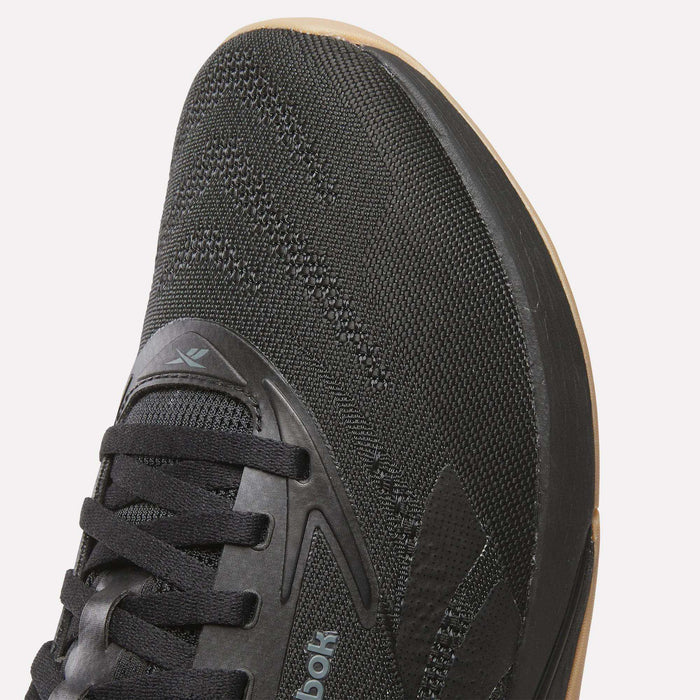 Close-up of the front and side of Reebok Nano X5 Training Shoes for men, featuring a black mesh upper, black laces, gum-colored sole edge, subtle branding, stitching accents, and comfort-focused design for training.