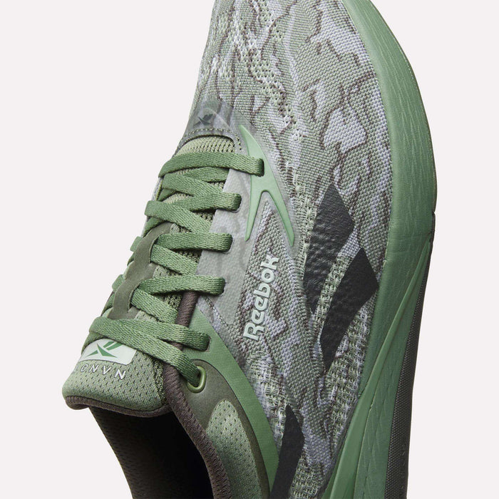 Close-up view of Reebok Nano X5 Training Shoes for men, featuring a green camouflage pattern, green laces, black Reebok logo, breathable mesh upper, and textured sole for comfort.