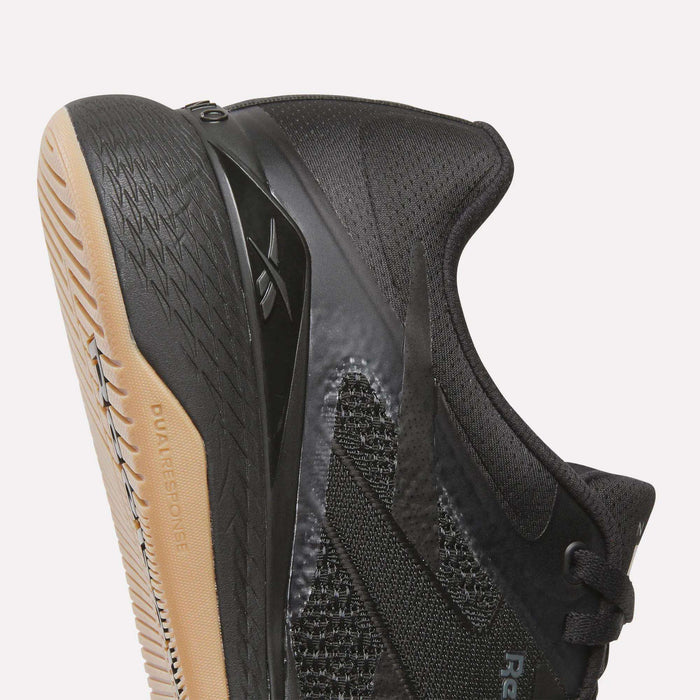 A close-up of the Reebok Nano X5 Training Shoes in black highlights the side and sole with "DUAL RESPONCE" text, a textured upper, and a gum-colored rubber outsole—engineered for comfort in every workout.