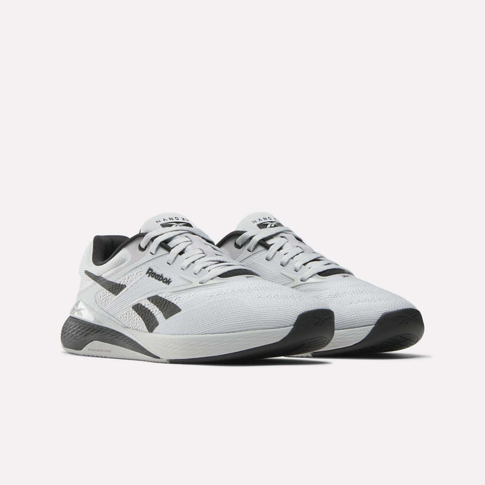 A pair of Reebok Nano X5 men’s training shoes in white with black accents, shown from the front on a white background. They feature mesh uppers, black outsoles, and the Reebok logo on the side.