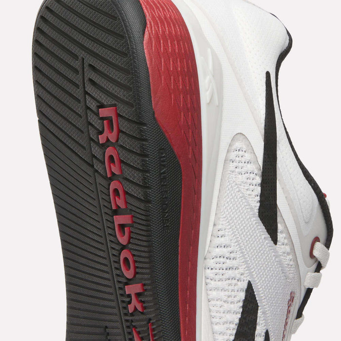 Close-up of the sole and side of Reebok Nano X5 Training Shoes, showing a textured black outsole with red Reebok branding, a white mesh upper, and bold red midsole—ideal for men’s training shoe collections.