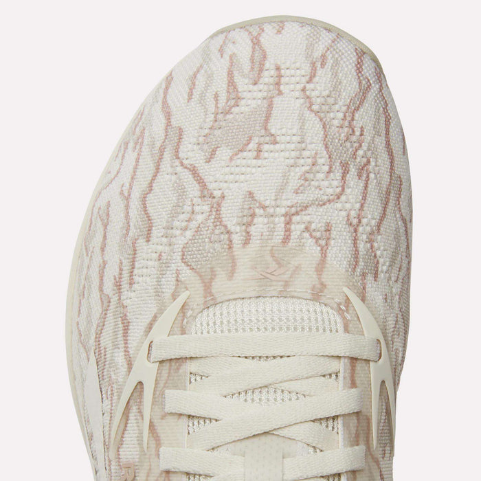 Close-up of the Reebok Nano X5 Training Shoes' toe area, showcasing textured, woven cream fabric with light pink wavy patterns and cream-colored laces through white eyelets.