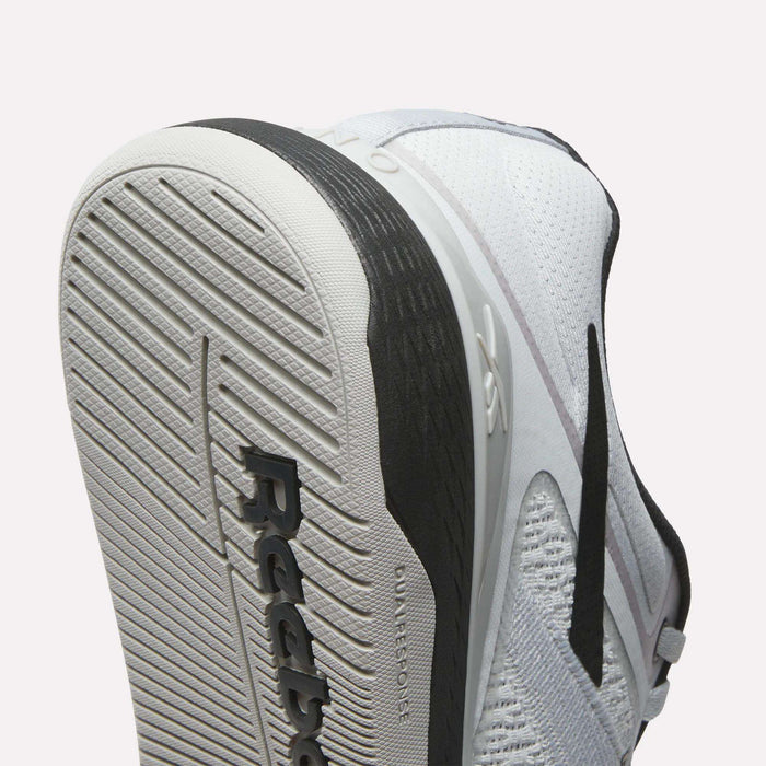 Close-up of the sole and side of a white Reebok Nano X5 Training Shoe, featuring black accents, textured tread pattern, and Reebok branding on the outsole.